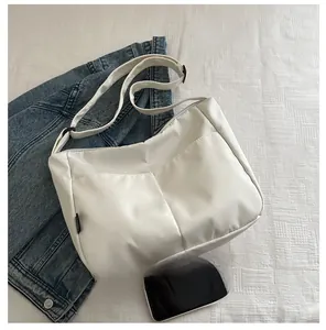 Detail view of compact white canvas crossbody bag with two front pockets and phone for size reference