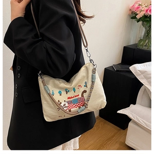 Detail of embroidered cat pattern and woven strap on a cream canvas shoulder bag