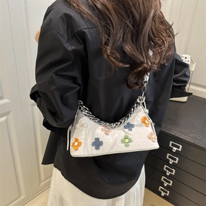 White baguette bag with floral accents and metal chain strap worn by a model