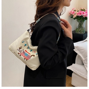 Close-up of cat embroidery and blue woven shoulder strap on a cream canvas tote bag