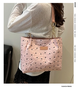 Close-up of pink quilted tote bag with black bow prints and golden chain strap detail