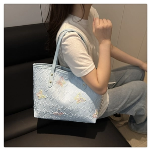 Détail d'un sac cabas bleu avec texture en losanges et broderies papillon colorées