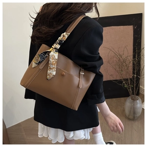 Brown leather tote bag detail with contrast stitching and decorative silk scarf on handle