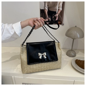Detail of woven straw handbag featuring black leather flap and silver bow clasp