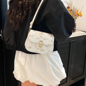 Sacoche blanche avec broderie florale et fermoir doré portée par un mannequin