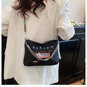 Detail of cartoon cat embroidery and colorful braided strap on black canvas bag