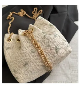 Detail of woven bucket bag featuring floral embroidery, pearl base, and gold chain strap