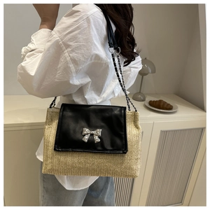 Detail of straw crossbody bag featuring black leather flap and silver bow clasp