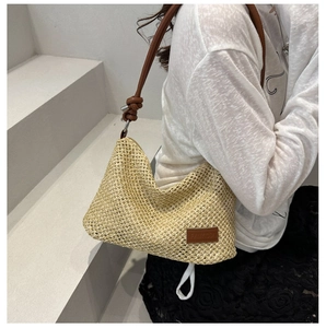Détail de la texture tissée et de la bandoulière en cuir brun d'un sac d'été en paille