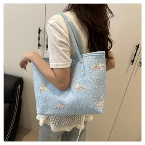 Détail d'un sac cabas bleu clair matelassé avec des papillons brodés et motifs de lettres