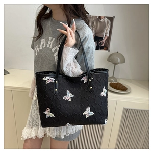 Détail du sac cabas noir avec broderie papillon et motifs monogrammes sur un modèle