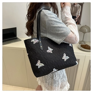 Détail d'un sac cabas noir avec gaufrage lettres E et broderies de papillons colorés