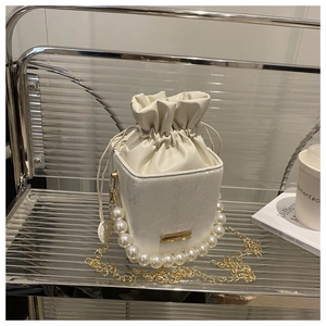 Close-up of cream white bucket bag featuring luxury pearl handle and gold chain strap