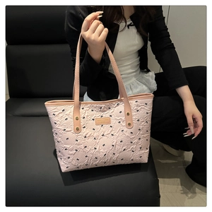 Rosa Shopper mit Schleifenmuster, geprägter Textur und Goldlogo auf grauem Sofa
