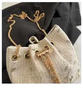 Close-up of golden chain strap and detailed woven texture on ivory bucket bag