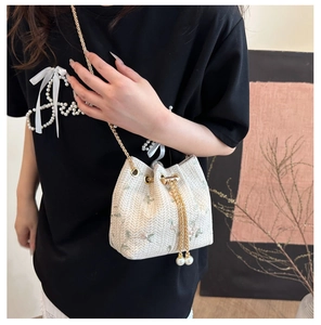 Detail of woven bucket bag featuring floral embroidery and pearl drawstring tassels