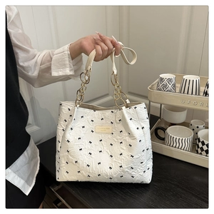 Detail of white tote bag featuring black bow patterns and gold chain handle detail