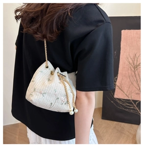 Close-up of woven bucket bag featuring floral embroidery, drawstring and pearl details