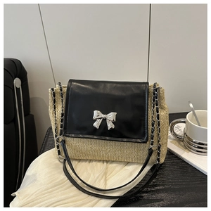 Close-up of the silver bow clasp on a beige straw crossbody bag with black leather flap