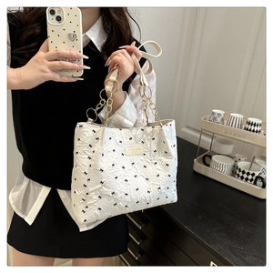 Detail view of white tote bag with black bow embroidery and gold chain handle