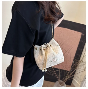 Close-up of woven bucket bag with floral embroidery and pearl chain detail