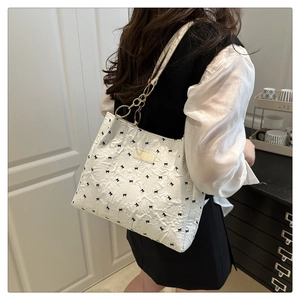 Close-up of white tote bag with black bows, pleated fabric, and gold hardware details