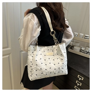 Detailed shoulder view of white quilted tote bag with black bow patterns and chain strap