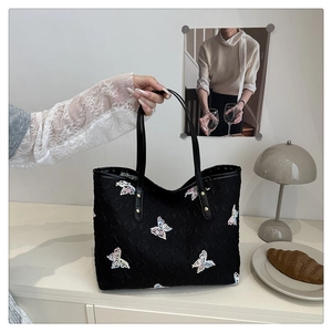 Détail du sac cabas matelassé noir avec broderies papillons colorées sur un bureau cosy