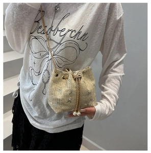 Close-up of woven bucket bag featuring floral embroidery, gold chain and pearl drawstring
