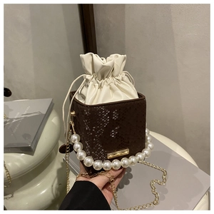 Detail of brown faux crocodile bucket bag with pearl handle and golden chain strap