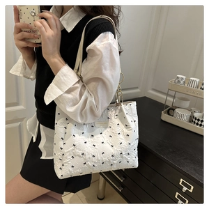 Detail of white quilted tote bag featuring black bow embroidery and gold chain strap