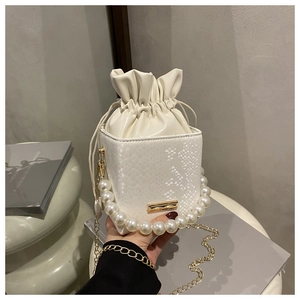 Detail of white bucket bag with snakeskin texture, pearl handle and gold chain strap