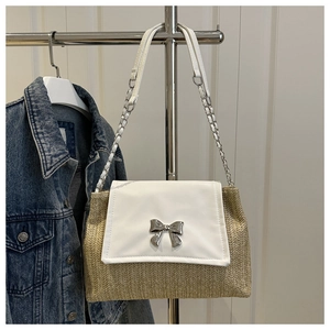 Close-up of woven straw handbag featuring a white leather flap and silver bow clasp