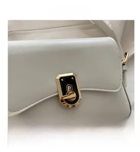 Detail of the white crossbody bag featuring a golden hardware clasp with black enamel inlay