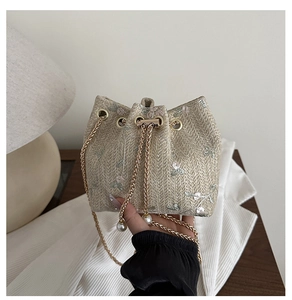 Detail of woven straw bucket bag with floral embroidery and elegant pearl accents