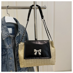 Detail of silver bow buckle on straw woven bag with black faux leather flap and chain strap