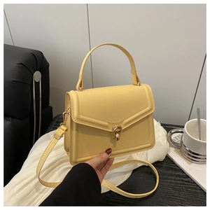 Detailed close-up of light yellow handbag featuring a gold turn-lock and adjustable strap