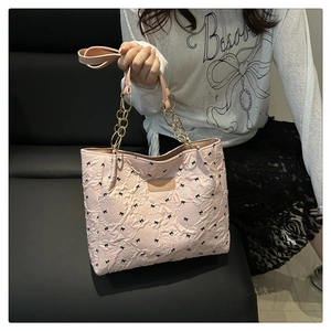 Detailed shot of a pink quilted tote bag with black bow patterns and chain strap
