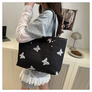 Détail du sac cabas matelassé noir avec broderies papillons colorées et logo gravé