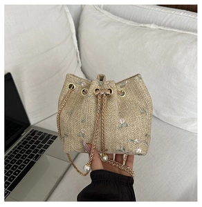 Detail of woven straw bucket bag with floral embroidery and pearl chain strap