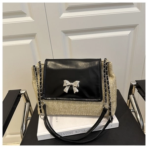 Detailed view of silver metal bow buckle on straw and black leather shoulder bag