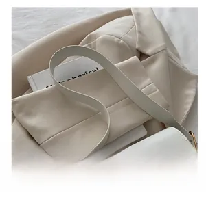 Detailed close-up of a white leather bag featuring a gold clasp on a beige blazer