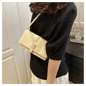 Détail du sac à bandoulière crème à texture tissée porté par un mannequin en intérieur