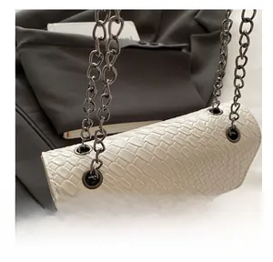 Close-up of white woven leather texture with gunmetal chain strap and buckle details