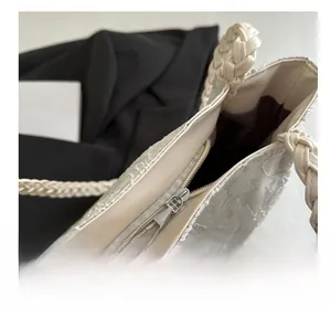 Detail view of smooth silver metal zipper and textured fabric on the white shoulder bag
