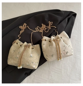 Detailed view of woven straw bucket bag with floral embroidery and pearl drawstring