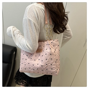 Detail of pink bow-print tote bag with unique gold chain shoulder strap on model