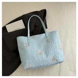 Détail du sac cabas bleu clair avec matelassage en losange et broderies papillon colorées