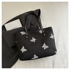 Gros plan sur un sac cabas matelassé noir avec broderies papillons et rivets métalliques