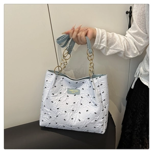 Detail of white tote bag with black bow pattern, gold chain link and blue leather handle